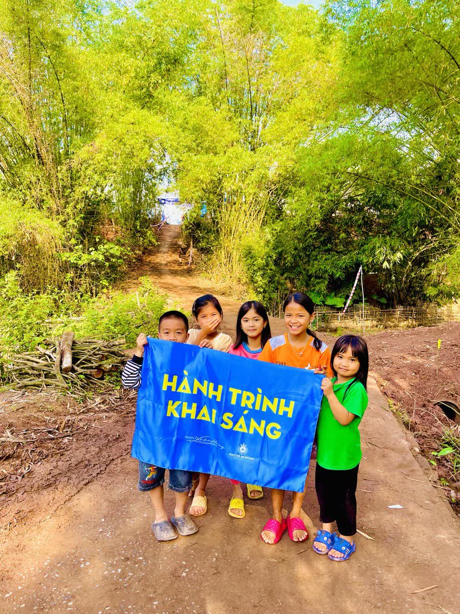 Năm em nhỏ cầm lá cờ Hành Trình Khai Sáng trên một con đường đất giữa rặng tre